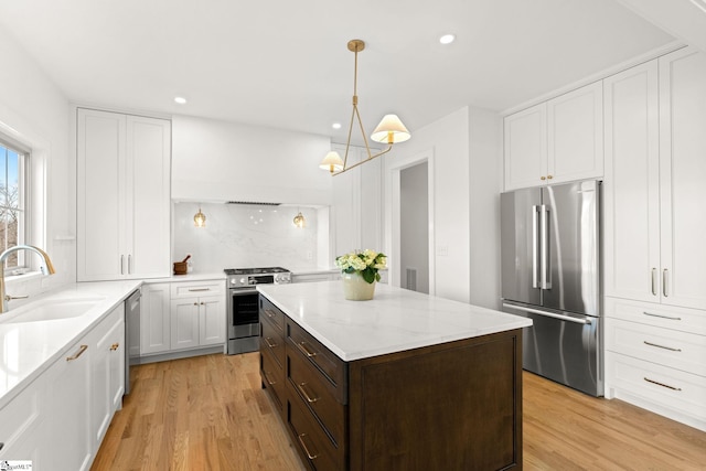 kitchen with dark brown cabinetry, sink, stainless steel appliances, light hardwood / wood-style floors, and decorative light fixtures