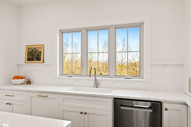 kitchen featuring dishwasher, sink, light stone countertops, tasteful backsplash, and white cabinetry