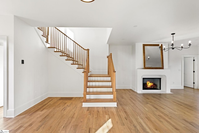 stairs with wood-type flooring and a notable chandelier