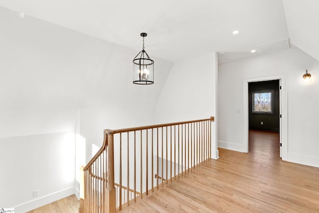 corridor with a notable chandelier, light hardwood / wood-style floors, and vaulted ceiling