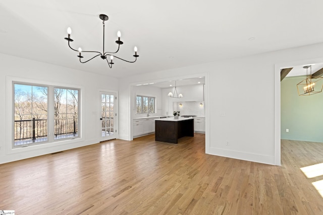 unfurnished living room with a chandelier and light wood-type flooring