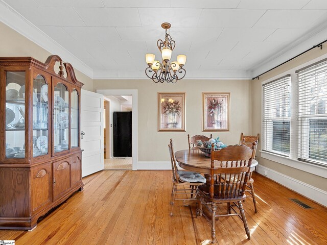 dining space featuring light wood-type flooring, ornamental molding, and an inviting chandelier