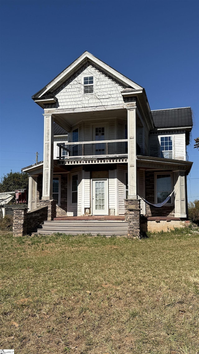 rear view of house featuring solar panels, a balcony, and a yard