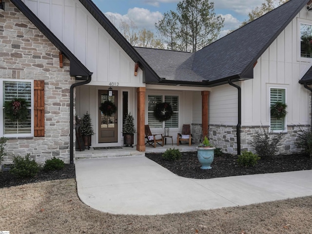 view of exterior entry with stone siding, covered porch, board and batten siding, and roof with shingles