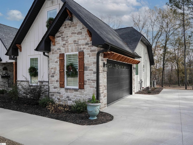 view of property exterior with driveway, stone siding, roof with shingles, an attached garage, and board and batten siding