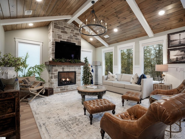 living room featuring a stone fireplace, beamed ceiling, light hardwood / wood-style floors, wood ceiling, and a chandelier