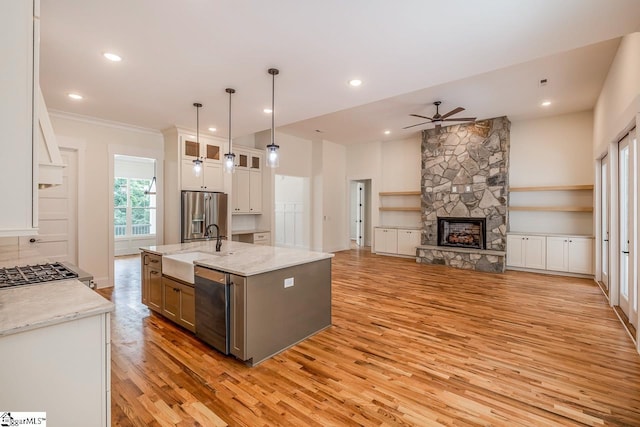 kitchen with a kitchen island with sink, light stone countertops, light wood-type flooring, white cabinetry, and stainless steel appliances