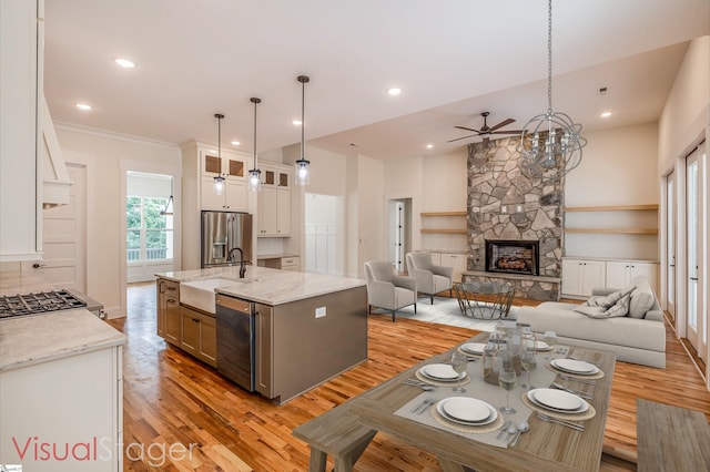 kitchen featuring white cabinetry, light stone countertops, a fireplace, a center island with sink, and appliances with stainless steel finishes