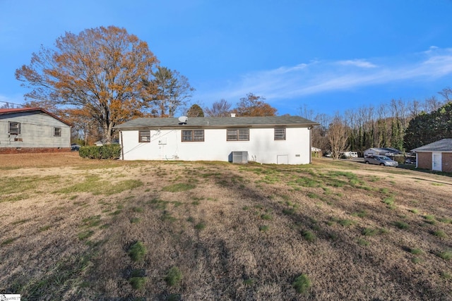 rear view of property with central air condition unit and a lawn