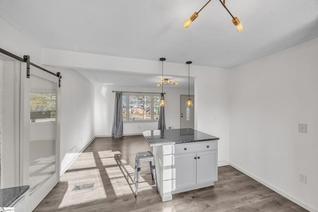 kitchen with dark stone countertops, hanging light fixtures, dark hardwood / wood-style floors, white cabinets, and a barn door