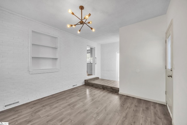 unfurnished living room with built in shelves, wood-type flooring, a chandelier, and brick wall