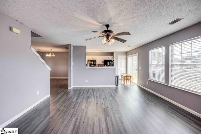 unfurnished living room featuring a textured ceiling, ceiling fan with notable chandelier, and dark wood-type flooring