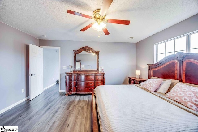 bedroom with ceiling fan, wood-type flooring, and a textured ceiling