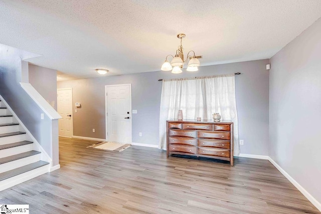 entryway with a notable chandelier, light wood-type flooring, and a textured ceiling