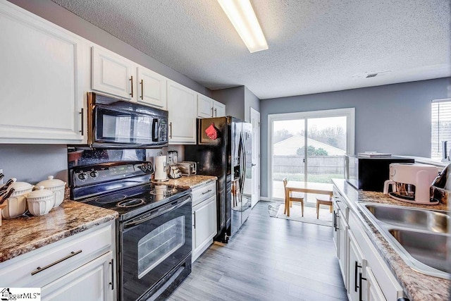 kitchen with black appliances, a healthy amount of sunlight, white cabinets, and light wood-type flooring