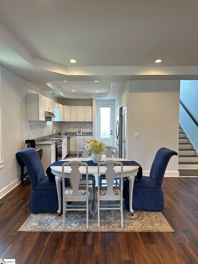 dining area featuring a raised ceiling, dark hardwood / wood-style flooring, and sink