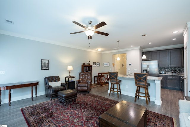 living room with crown molding, dark hardwood / wood-style flooring, ceiling fan, and sink