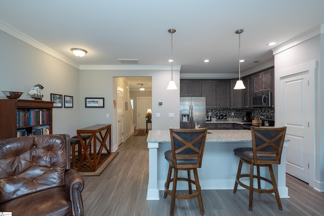 kitchen featuring dark brown cabinetry, hanging light fixtures, stainless steel appliances, decorative backsplash, and a breakfast bar