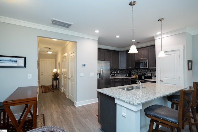 kitchen with appliances with stainless steel finishes, a kitchen island with sink, sink, decorative light fixtures, and light hardwood / wood-style flooring