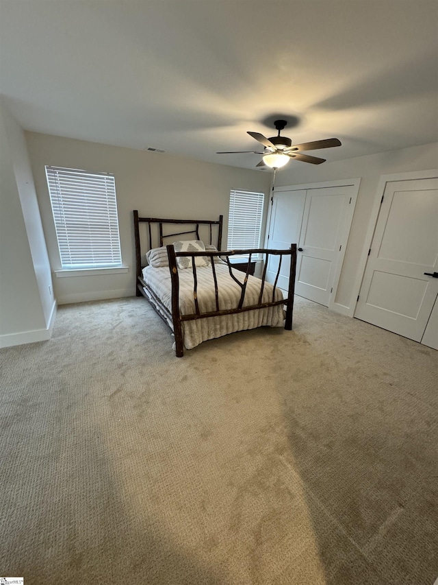 bedroom featuring two closets, light colored carpet, and ceiling fan