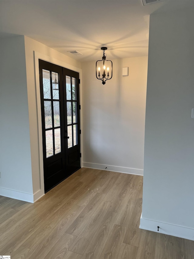 foyer entrance with french doors, a chandelier, and light hardwood / wood-style flooring