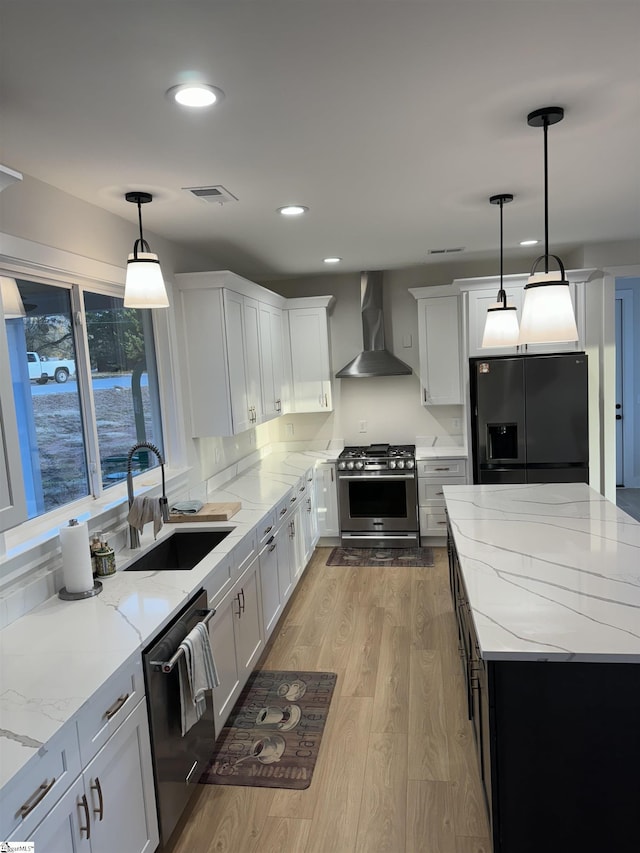 kitchen featuring appliances with stainless steel finishes, pendant lighting, white cabinetry, sink, and wall chimney range hood