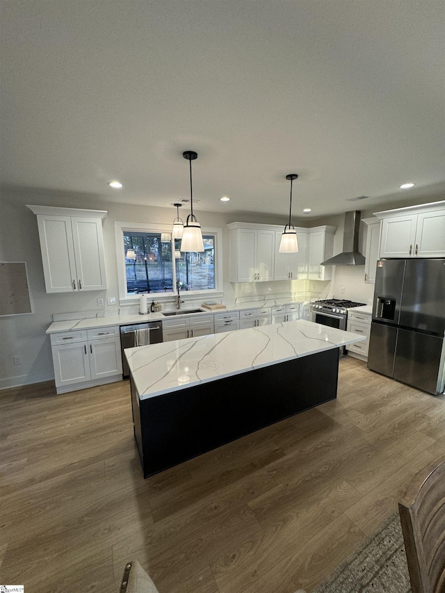 kitchen featuring wall chimney exhaust hood, stainless steel appliances, hanging light fixtures, and a kitchen island