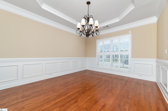 spare room with hardwood / wood-style floors, an inviting chandelier, a raised ceiling, and crown molding