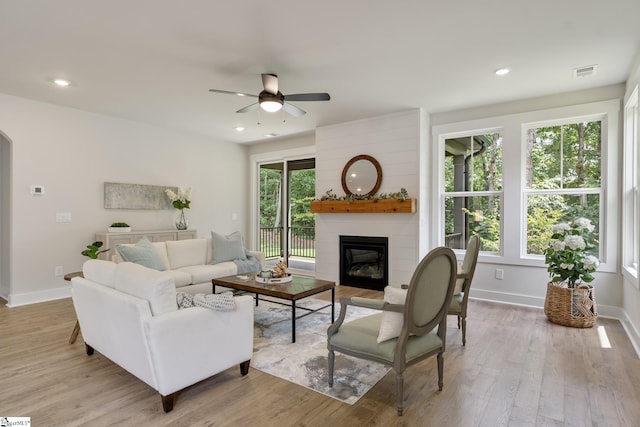 living room with ceiling fan, a large fireplace, and light hardwood / wood-style floors