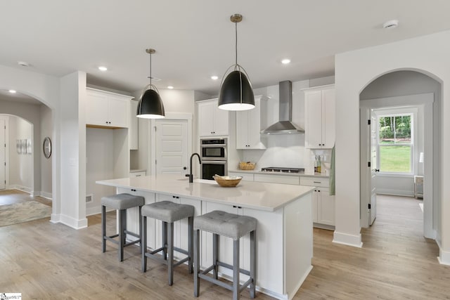 kitchen featuring pendant lighting, white cabinetry, wall chimney exhaust hood, and an island with sink