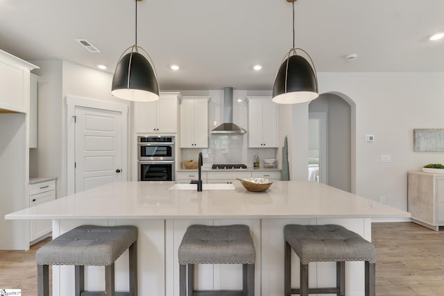 kitchen featuring stainless steel double oven, wall chimney exhaust hood, sink, and pendant lighting