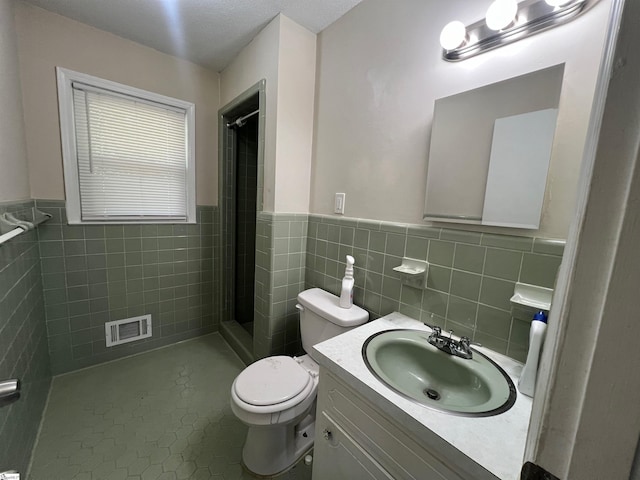 bathroom featuring vanity, tile patterned floors, toilet, tile walls, and a tile shower