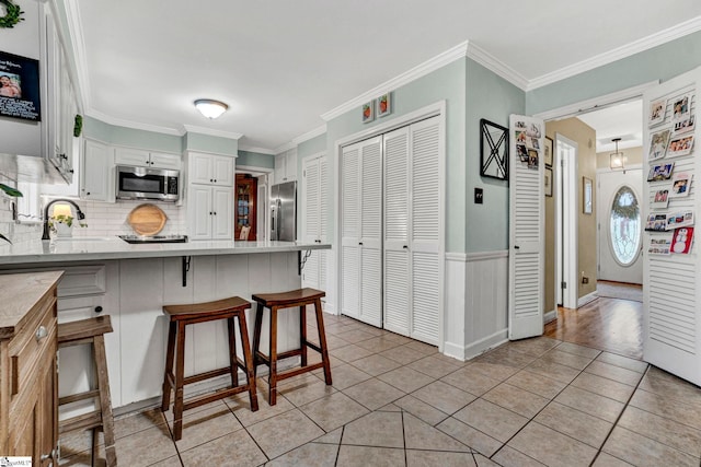 kitchen with white cabinetry, tasteful backsplash, a breakfast bar, appliances with stainless steel finishes, and ornamental molding