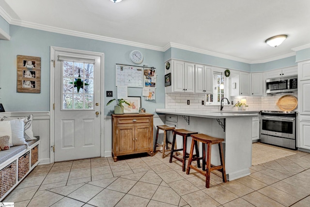 kitchen featuring white cabinets, crown molding, appliances with stainless steel finishes, a kitchen bar, and kitchen peninsula