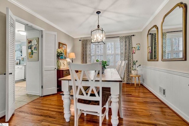 dining room featuring an inviting chandelier, ornamental molding, a textured ceiling, and light wood-type flooring