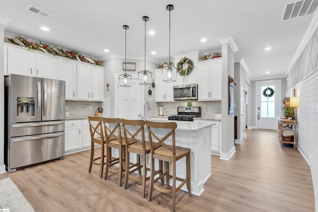 kitchen featuring a center island with sink, decorative light fixtures, white cabinets, and appliances with stainless steel finishes