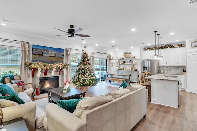 living room featuring ceiling fan, sink, ornamental molding, and light wood-type flooring