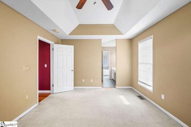 empty room with light carpet, a textured ceiling, a tray ceiling, and ceiling fan