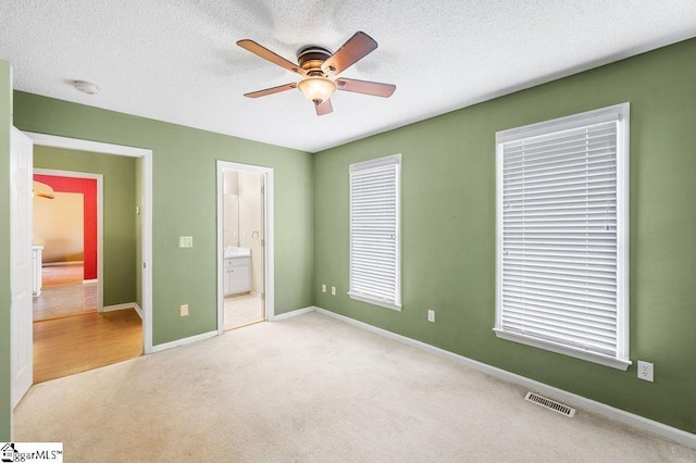 unfurnished bedroom featuring ensuite bath, ceiling fan, light colored carpet, and a textured ceiling