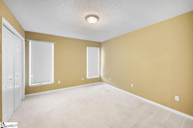 unfurnished bedroom featuring light colored carpet, a textured ceiling, and a closet