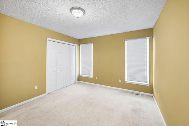 unfurnished bedroom with a textured ceiling, light colored carpet, and a closet