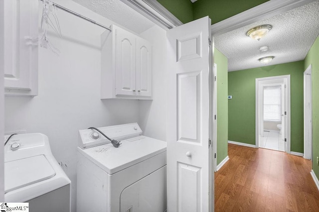 laundry room featuring cabinets, hardwood / wood-style floors, a textured ceiling, and separate washer and dryer