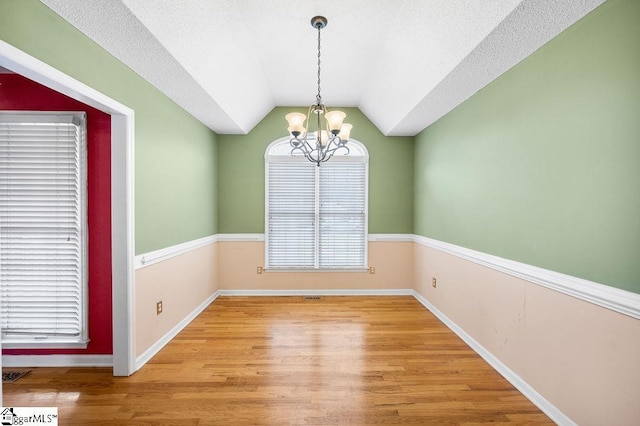 unfurnished dining area featuring wood-type flooring, lofted ceiling, a textured ceiling, and a chandelier