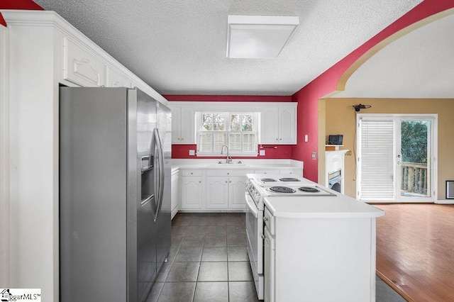 kitchen with white electric range oven, stainless steel fridge, a kitchen island, and white cabinetry