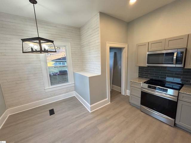 kitchen with gray cabinetry, hanging light fixtures, appliances with stainless steel finishes, light hardwood / wood-style floors, and a chandelier