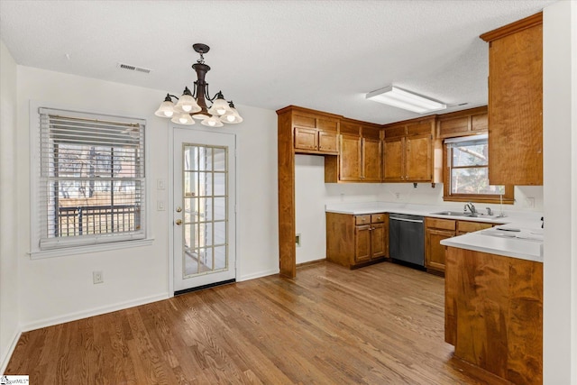 kitchen featuring visible vents, a sink, light wood-style floors, stainless steel dishwasher, and brown cabinets