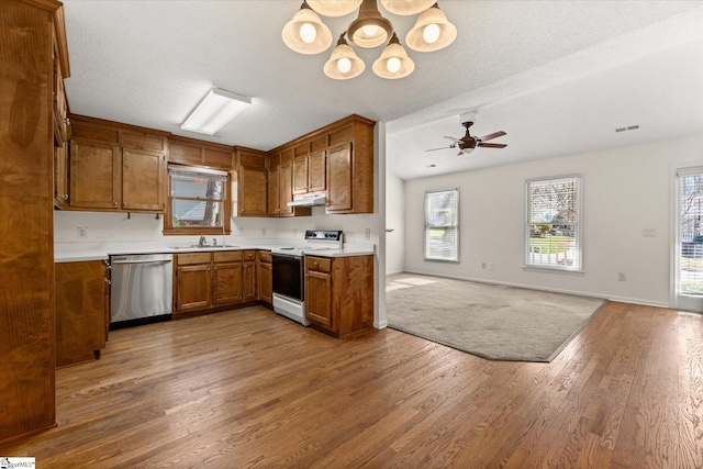 kitchen with brown cabinetry, a sink, electric stove, stainless steel dishwasher, and open floor plan