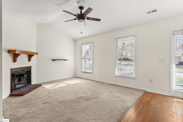 unfurnished living room with visible vents, lofted ceiling, a fireplace, a textured ceiling, and a ceiling fan