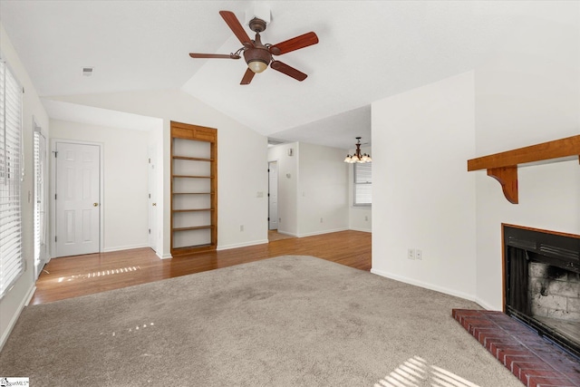 unfurnished living room with a brick fireplace, baseboards, carpet, lofted ceiling, and ceiling fan with notable chandelier