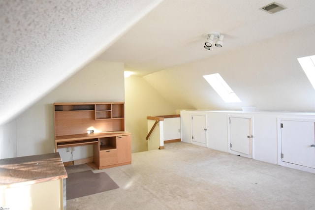 additional living space featuring vaulted ceiling with skylight, light colored carpet, visible vents, and a textured ceiling